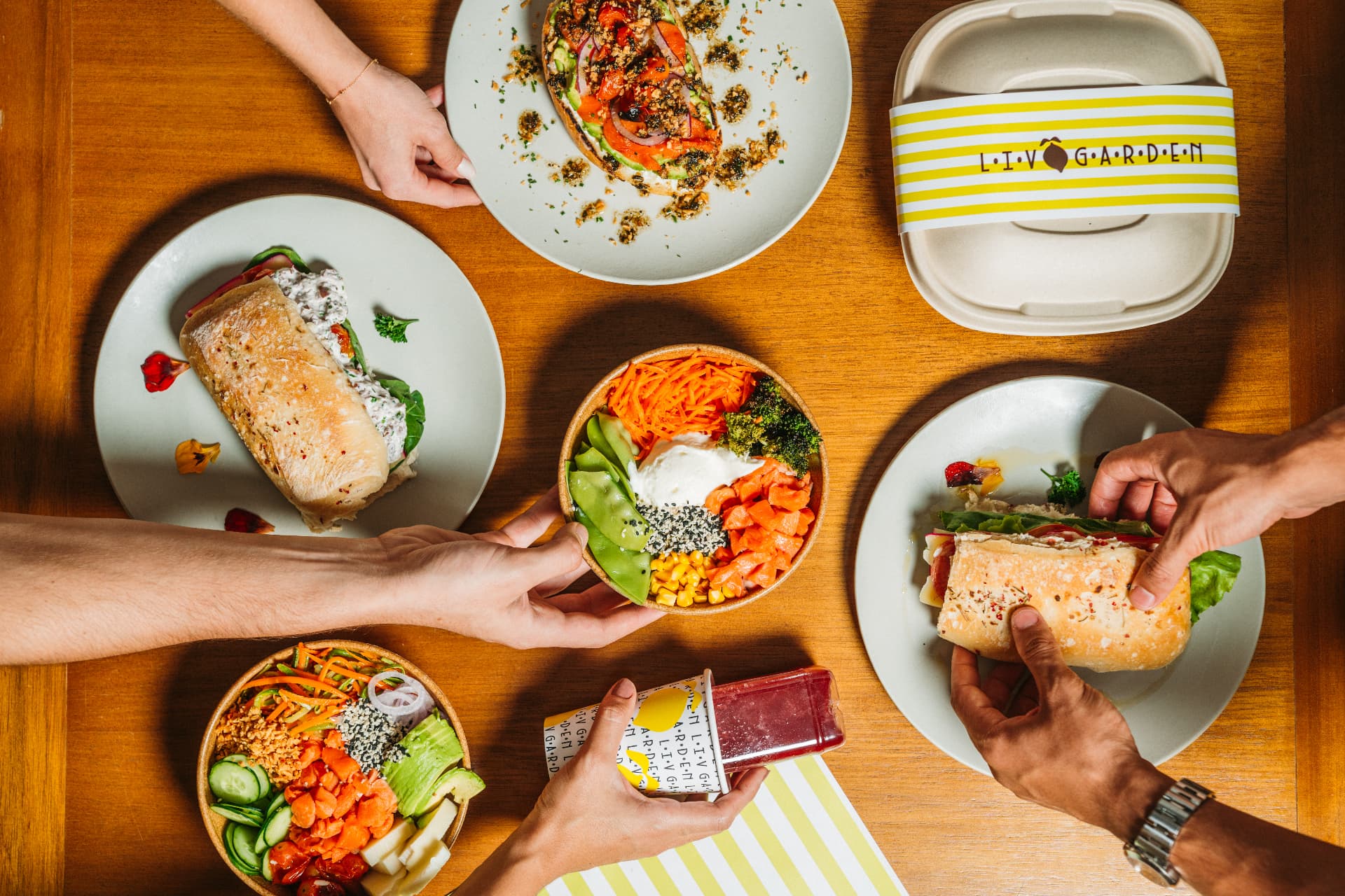 Mesa compartilhada da Liv Garden com bowls, sanduíches, suco e embalagem biodegradável da marca